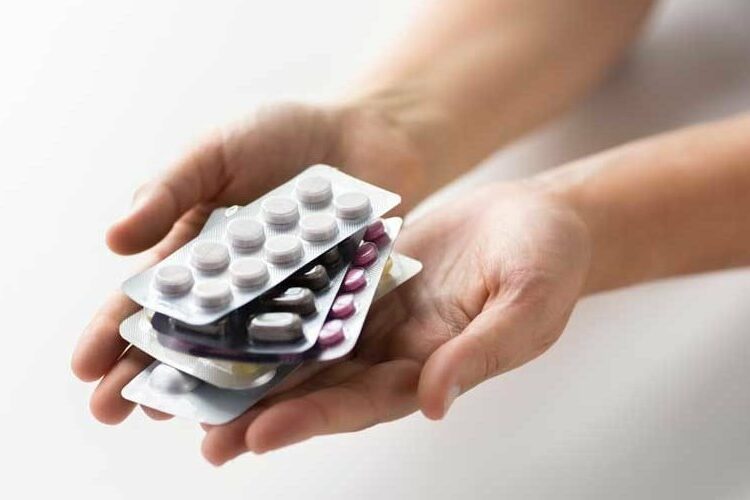 Hände halten mehrere Blisterverpackungen mit unterschiedlichen Tabletten in verschiedenen Farben.