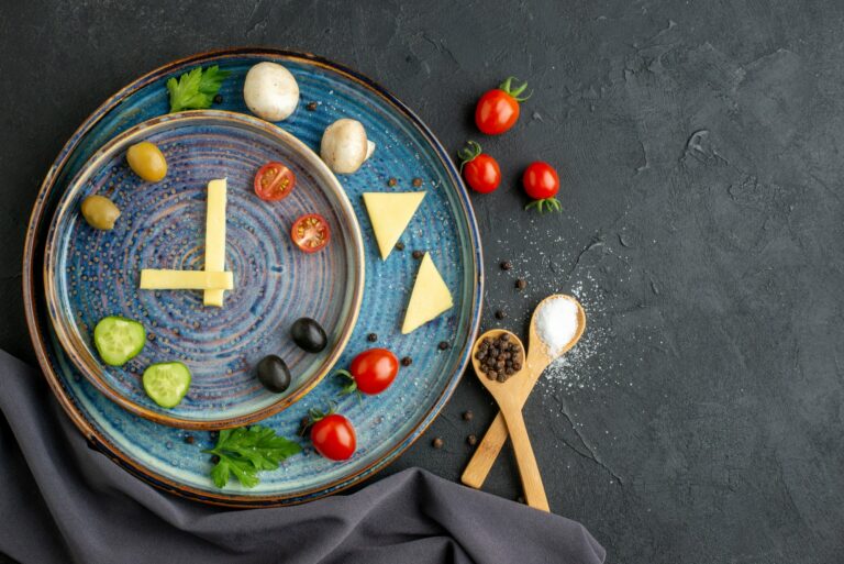 Ein kreativ angerichteter Teller mit Gemüse, Käse und Gewürzen in Form einer Uhr auf blauem Geschirr.