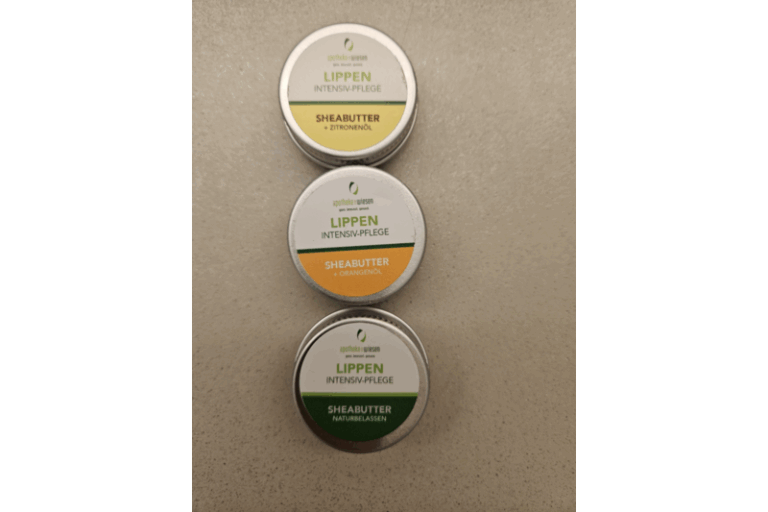 Drei Dosen Lippenpflege mit Sheabutter, inklusive Sorten mit Zitronen- und Orangenöl sowie einer natürlichen Variante.