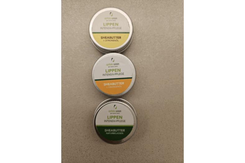 Drei Dosen Lippenpflege mit Sheabutter, inklusive Sorten mit Zitronen- und Orangenöl sowie einer natürlichen Variante.