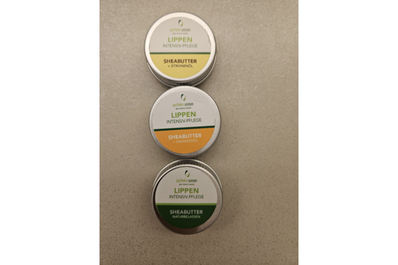 Drei Dosen Lippenpflege mit Sheabutter, inklusive Sorten mit Zitronen- und Orangenöl sowie einer natürlichen Variante.
